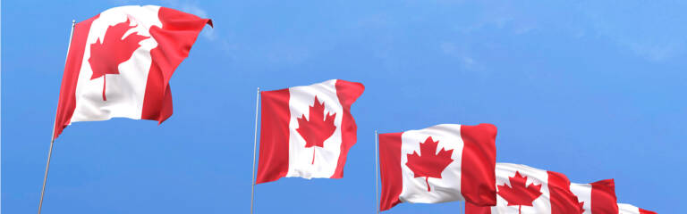 Image of multiple Canada Flags waving in front of a blue sky