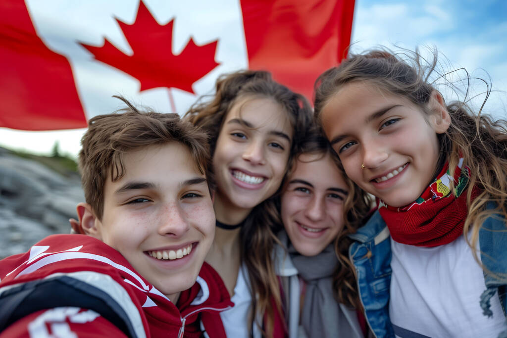 Image of People immigrating to Canada. 2 females and 2 makes standing in front of a Canada Flag
