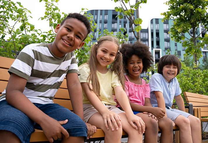 Image of multicultural children sitting on a bench smiling